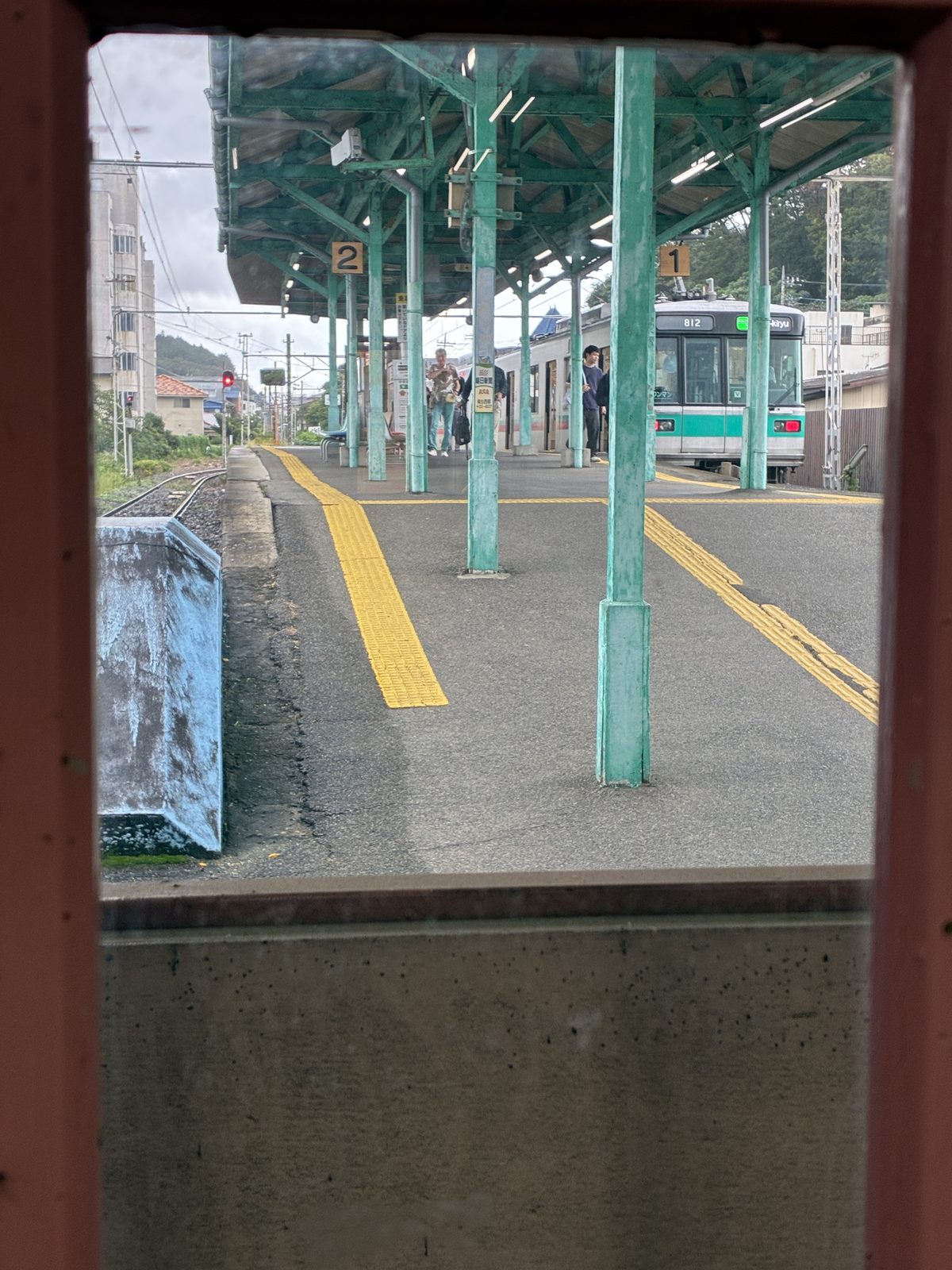西桐生駅の待合室の赤茶色の窓枠ごしに見た、ホームと上毛電鉄 800 型